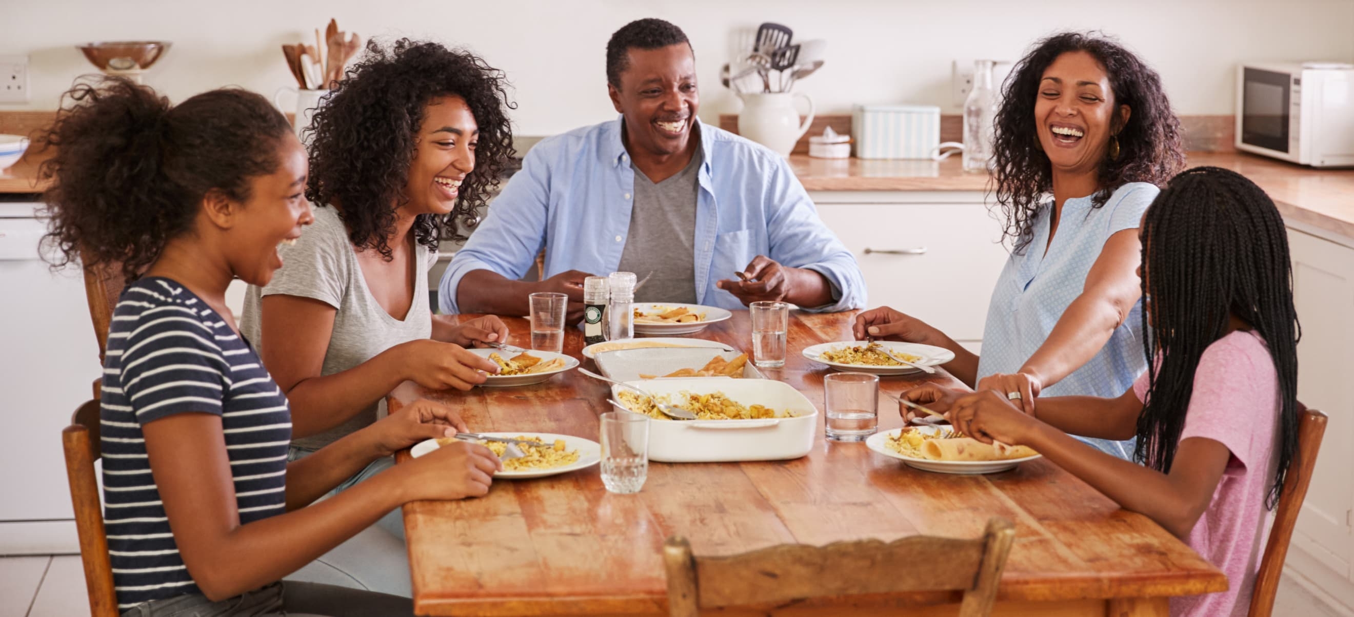 A family of five sits around a wooden dining table, laughing and eating a meal together in a bright kitchen, offering a perfect case study of joyful, everyday moments enhanced by the McCormick app.