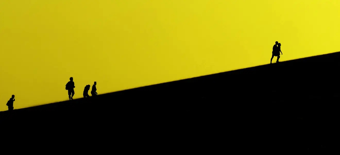 Black and yellow illustration displaying the silhouettes of a group of people climbing a hill.