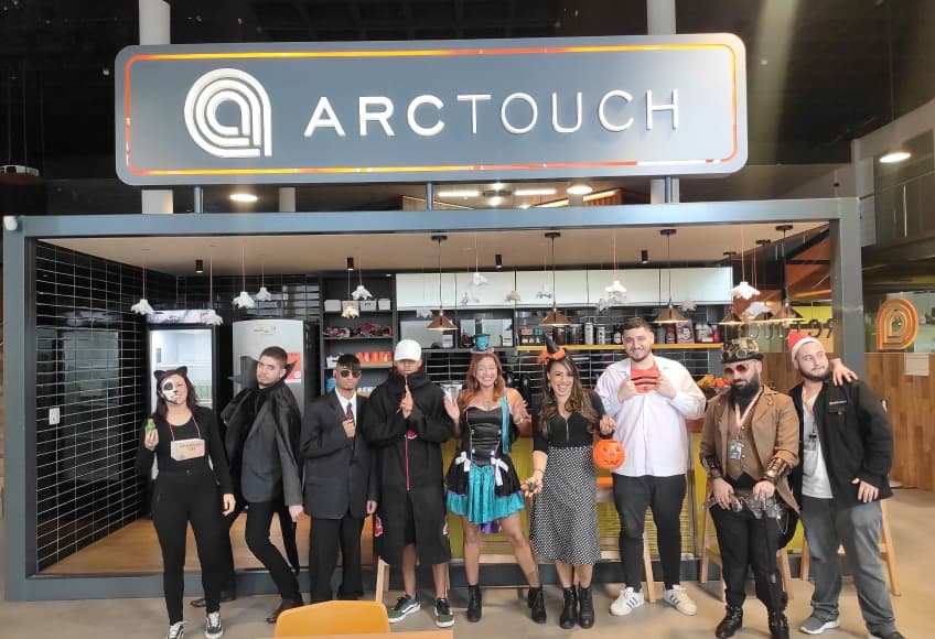 A group of people in costumes stands in a row in front of an "ARCTOUCH" sign.