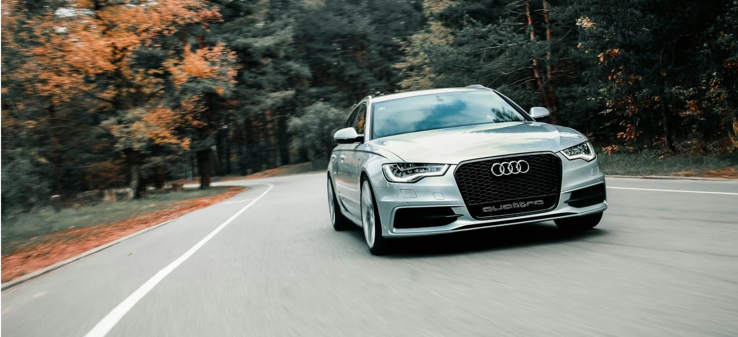An Audi virtual test drive app, driving on a curved, tree-lined road. The vehicle is in motion and centered in the image.