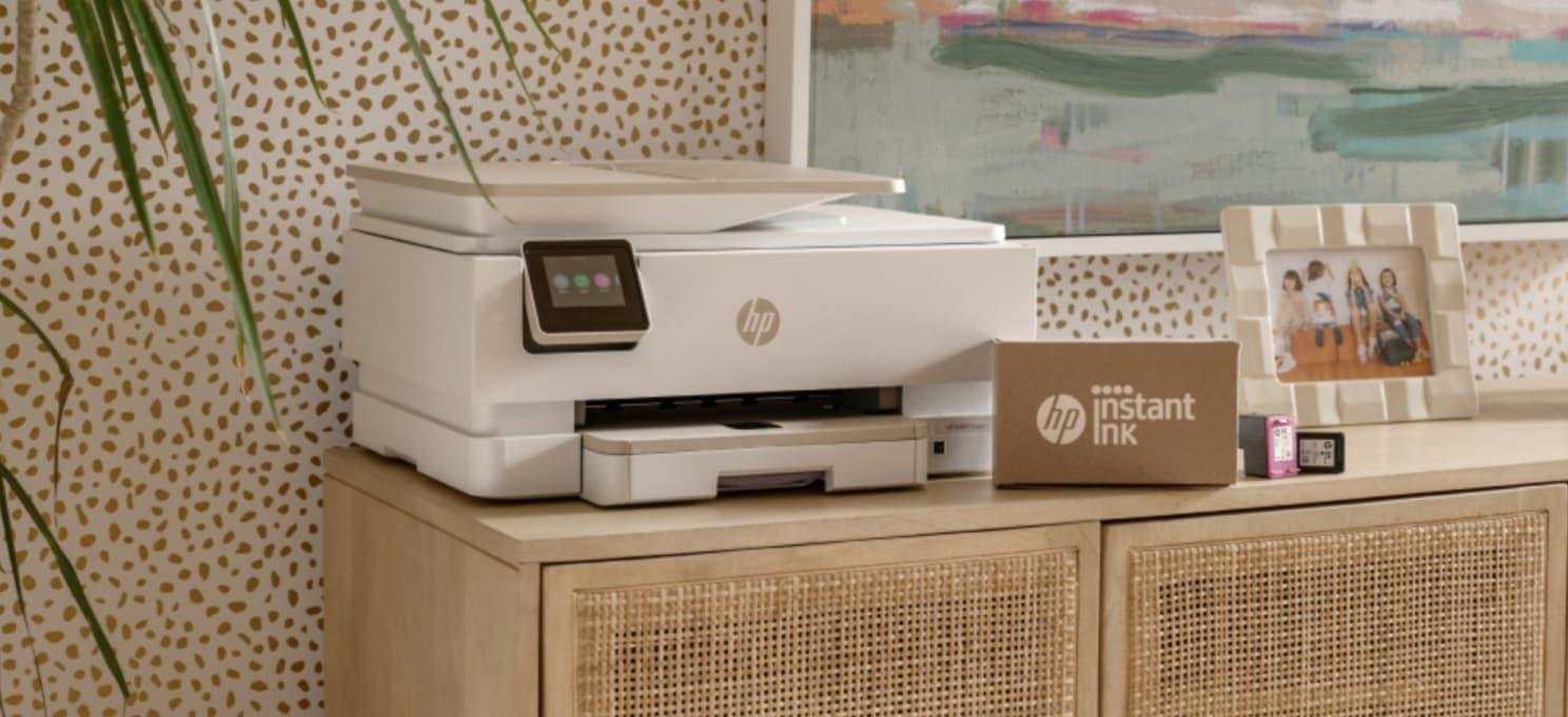 A white HP printer is on a wooden cabinet beside a cardboard box labeled "HP Instant Ink app" and ink cartridges, reflecting the tools of a successful company case study by ArcTouch.