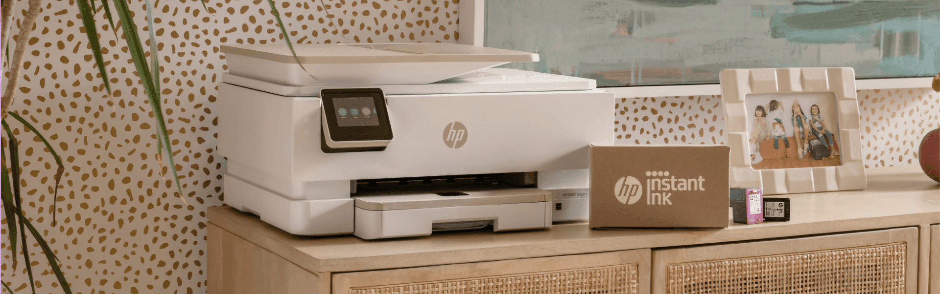 A white HP printer is on a wooden cabinet beside a cardboard box labeled "HP Instant Ink app" and ink cartridges, reflecting the tools of a successful company case study by ArcTouch.