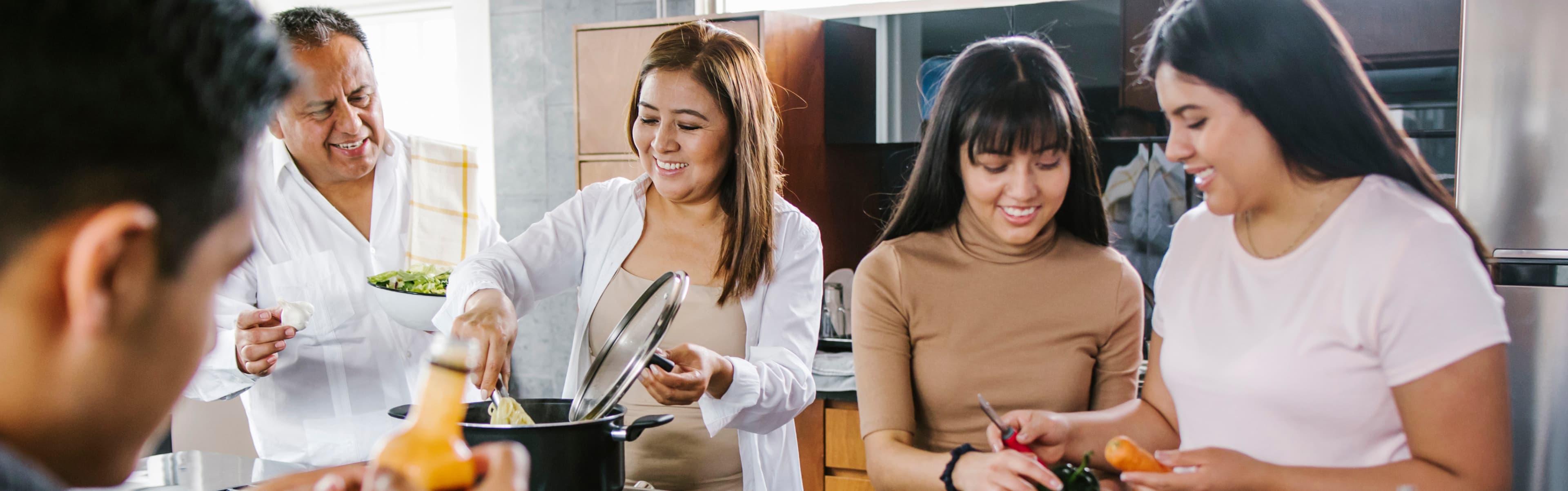 Three people cooking together in a kitchen, with one person standing nearby holding a plate—a perfect scene for a culinary case study using the McCormick app by ArcTouch.