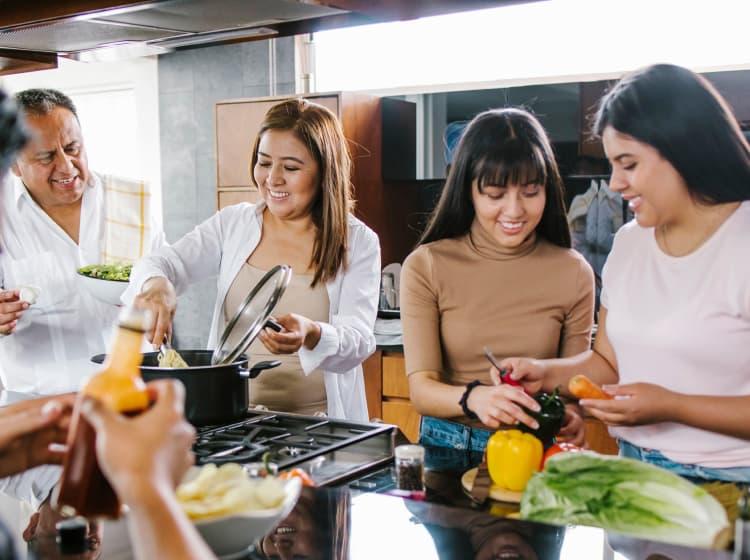Three people cooking together in a kitchen, with one person standing nearby holding a plate—a perfect scene for a culinary case study using the McCormick app by ArcTouch.