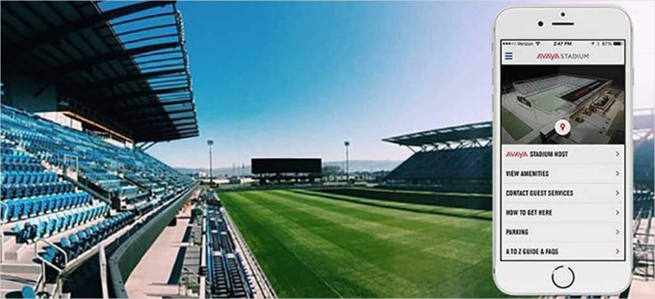 View of Avaya Stadium's interior with empty stands and a green field. An iPhone in the foreground displays the Avaya Stadium mobile app, efficiently built using Xamarin by ArcTouch, showcasing options for navigating the stadium.