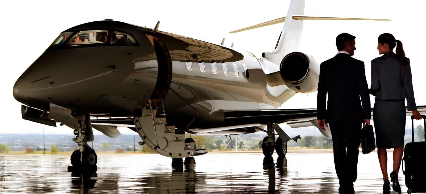 Two individuals in business attire walk towards a private jet, carrying luggage. The Honeywell jet is parked in an open hangar with a clear sky in the background.