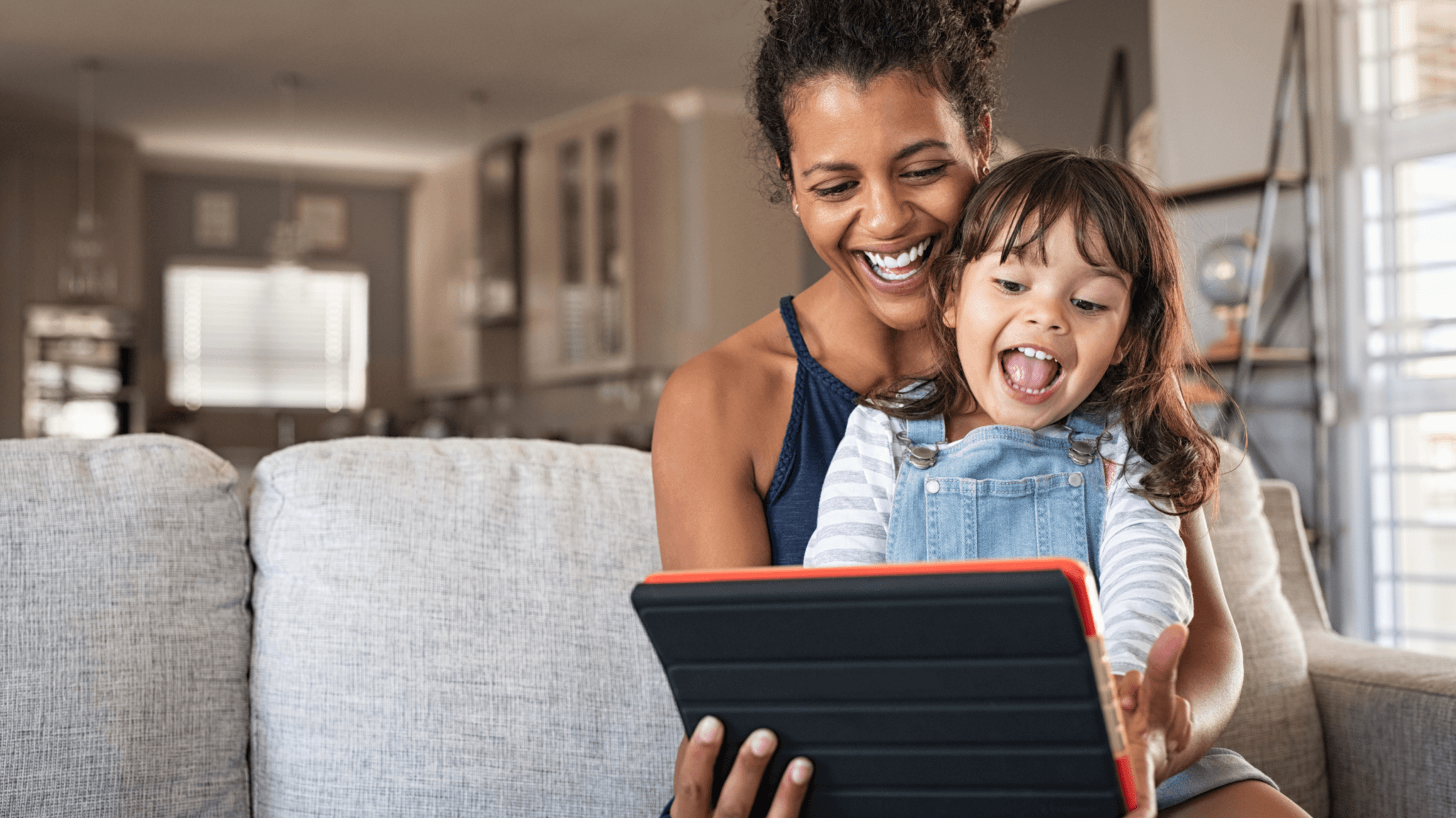 A woman and child sitting on a couch, smiling and looking at a tablet. They are enjoying ArcTouch's Common Sense Media app.