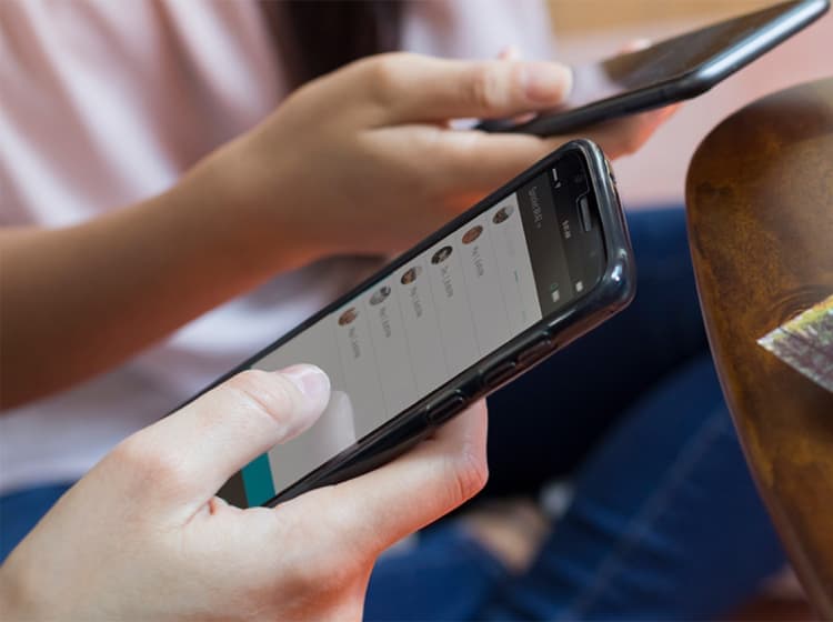 Two people use their smartphones next to an HP Sprocket app that is printing a picture on a wooden table.