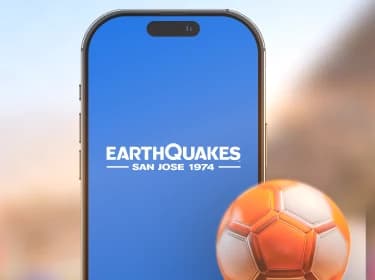 Blurred picture of Avaya Stadium's interior in the background. In the foreground, a soccer ball and an iPhone displaying the Earthquake mobile app, built with Xamarin by ArcTouch.