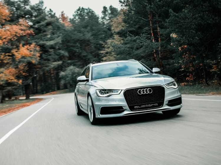 An Audi virtual test drive app, driving on a curved, tree-lined road. The vehicle is in motion and centered in the image.