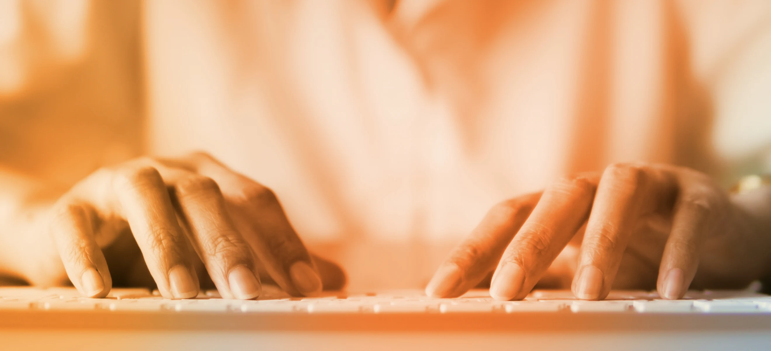 Orange-tinted close-up of a person's hands typing on a keyboard