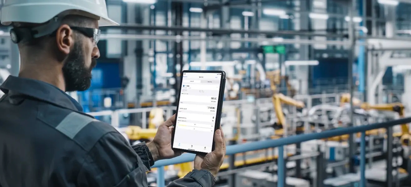 A man dressed in protective work clothing using a tablet to operate the SoloCUE® Flow Device Manager app in an industrial environment.