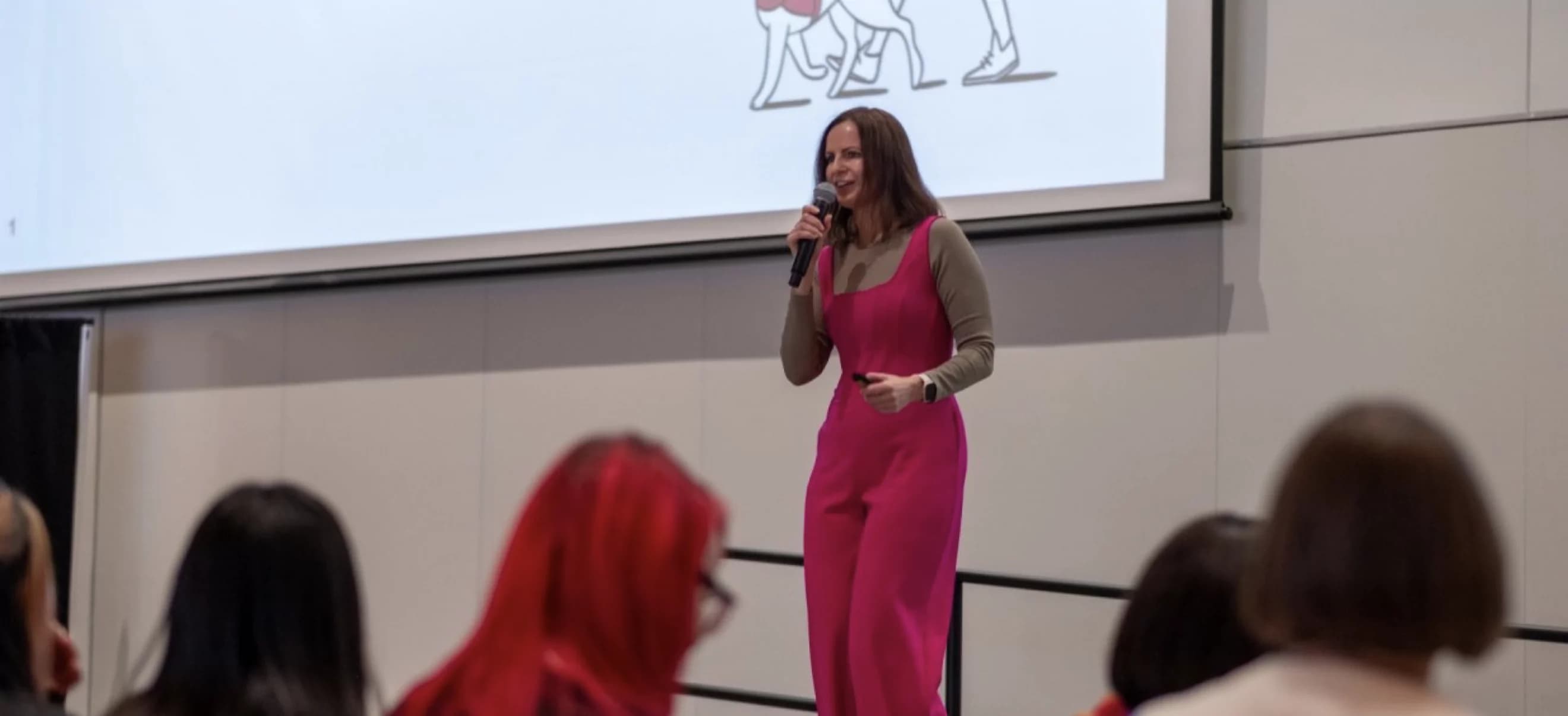 Fable accessibility leader, Kate Kalcevich, holding a microphone in front of a projected slide and speaking to a female audience