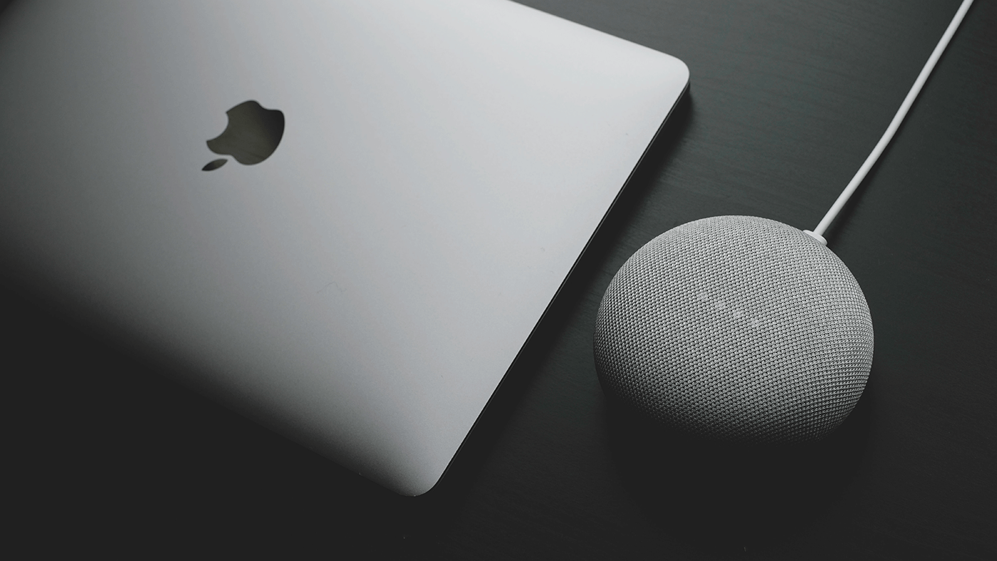 a Google Home device next to a MacBook used by a developer creating a Google Action